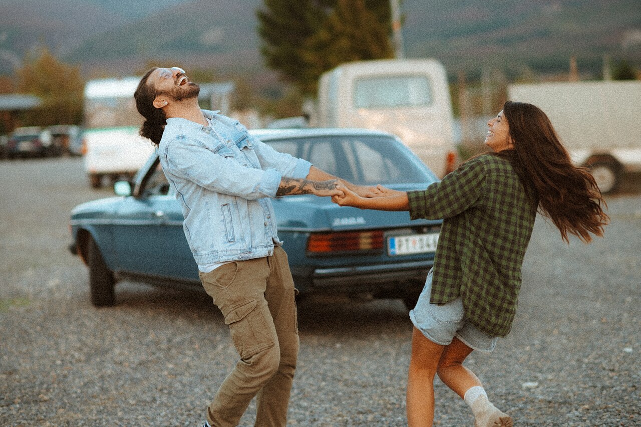 Two adults laughing and playfully pulling on each other's hands outdoors