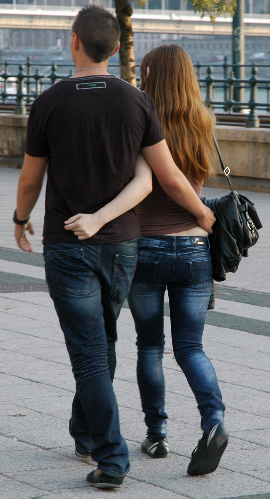 Two people walking outdoors with one person's arm around the other's waist