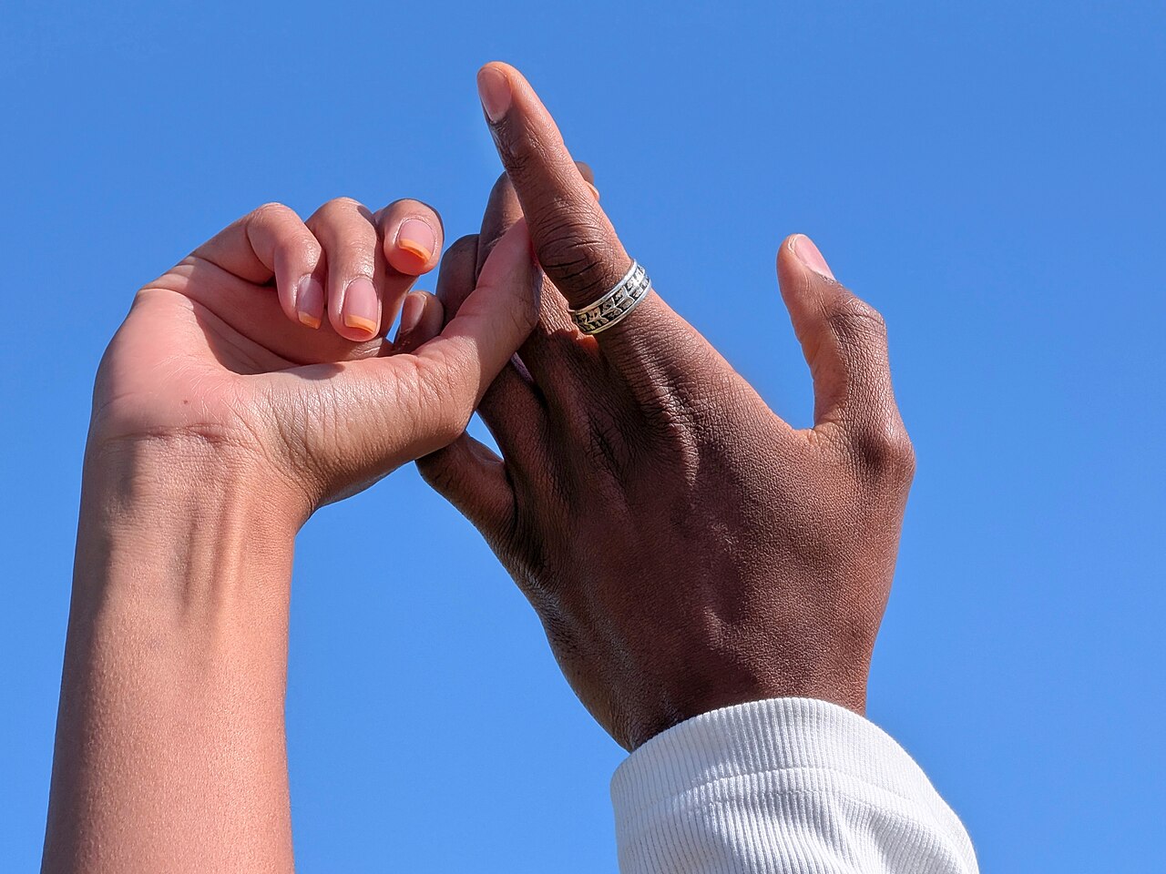 Two hands clasped, one wearing a ring