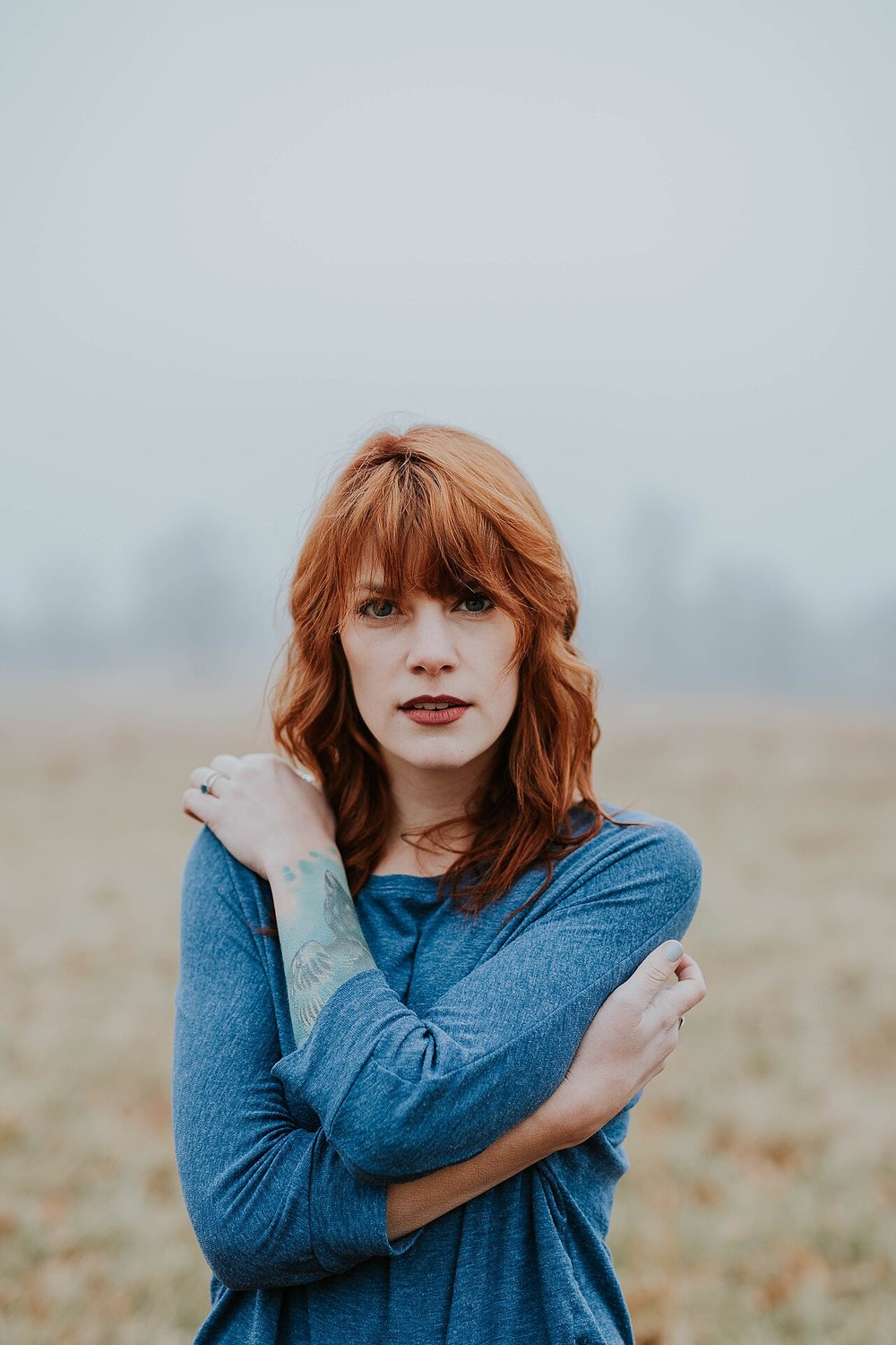 A woman standing with her arms folded in a misty field